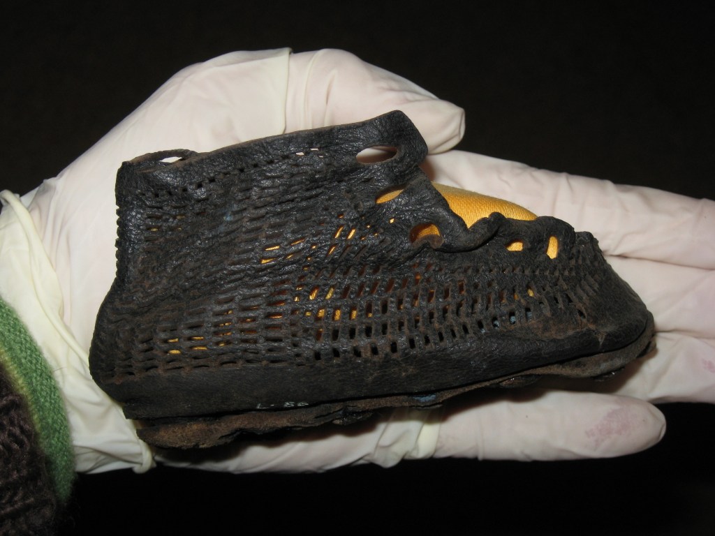 A small leather shoe for a baby, with a distinct fishnet pattern. 