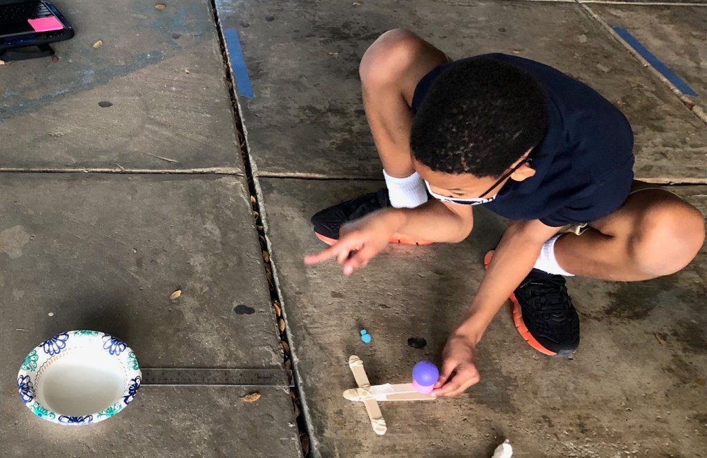 Student trying to launch a mini ball from a mini-catapult into a bowl.