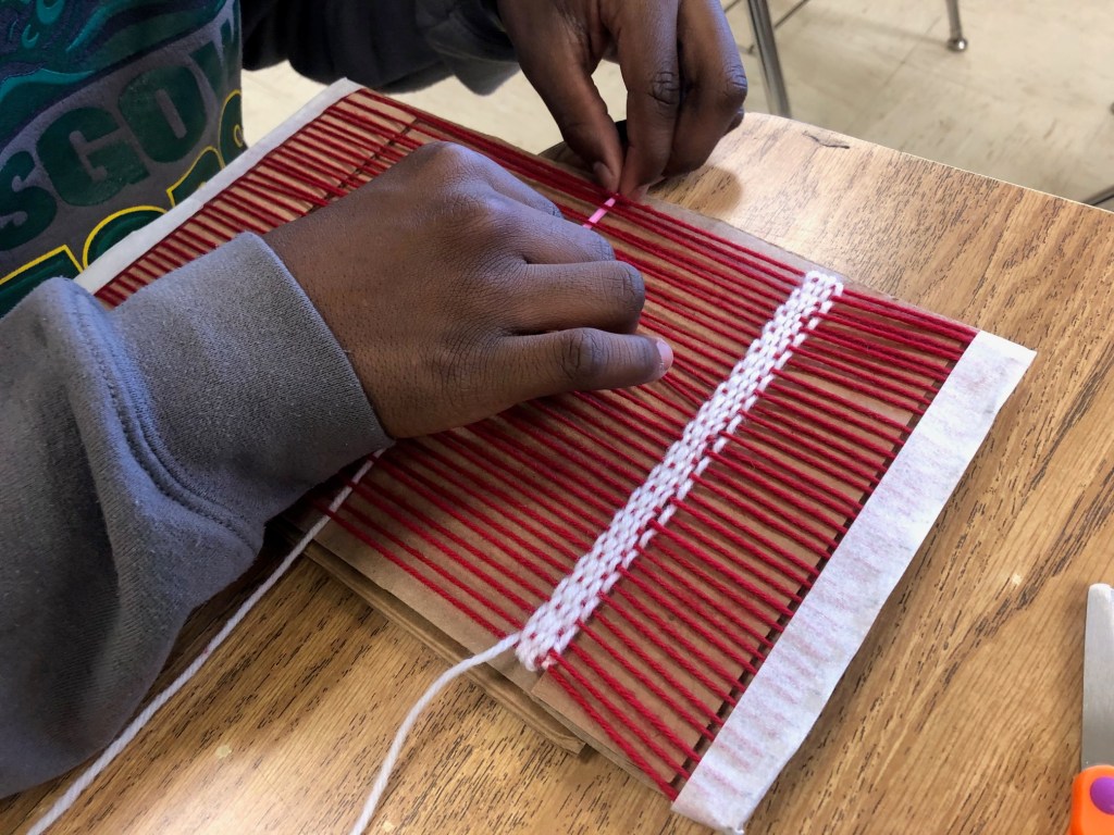 Image displaying the hands of a student trying out a cardboard loom