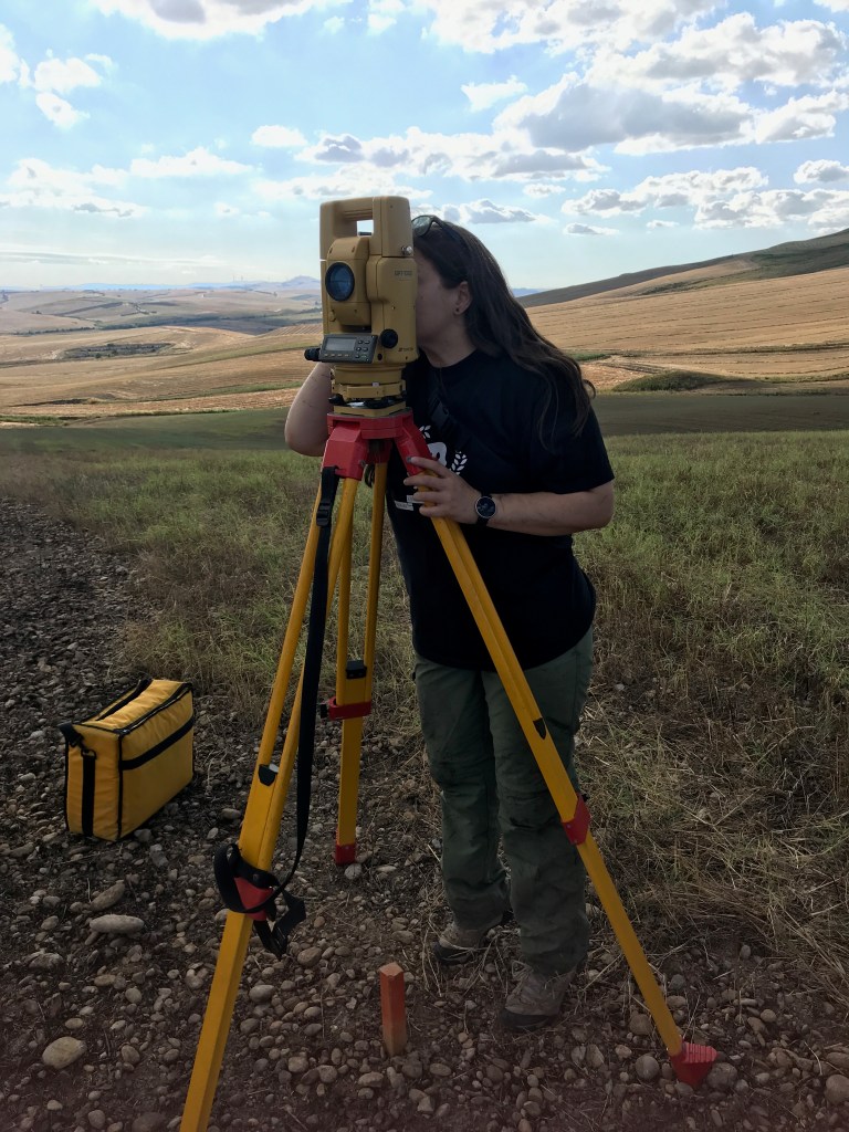 Dr. Liana Brent surveying while looking into a total station. 