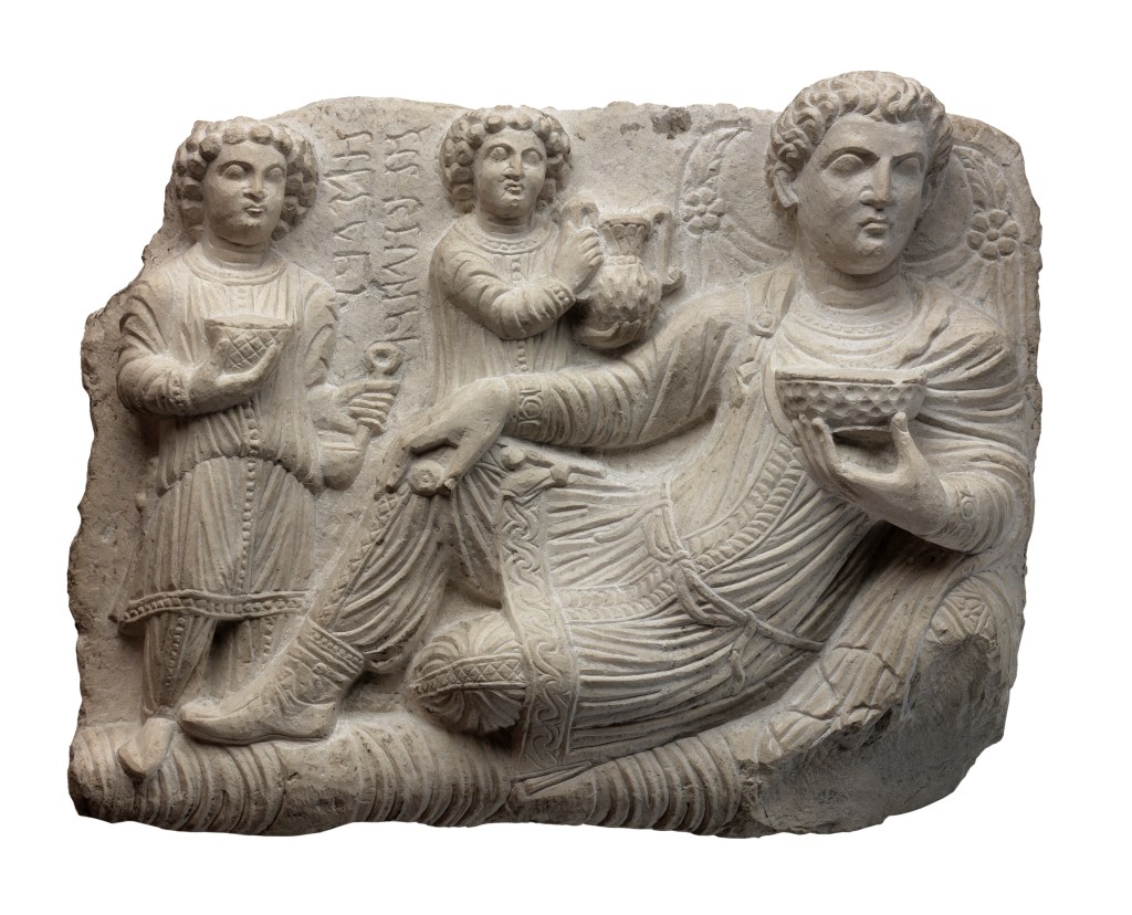 Relief stele of a reclining man in the foreground, with two smaller attendants carrying vessels at his feet. 