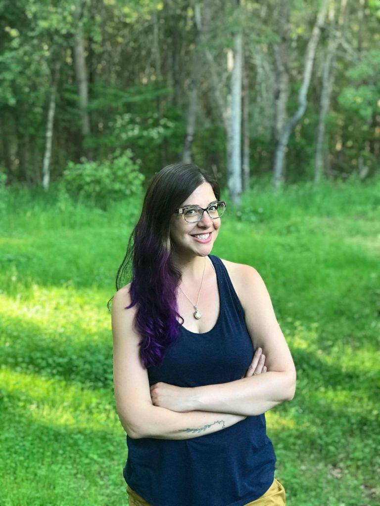 Photo of Dr. Chelsea Gardner standing in a field with trees in the background. 