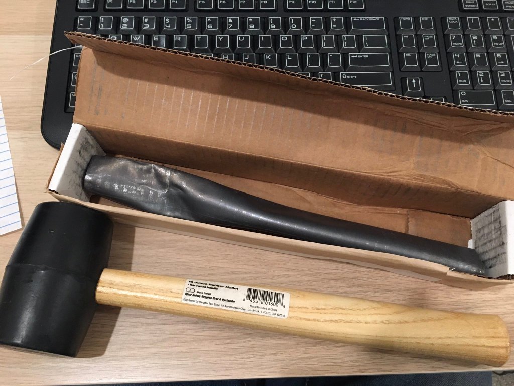 A modern lead curse tablet in a box with a mallet in front of it. 