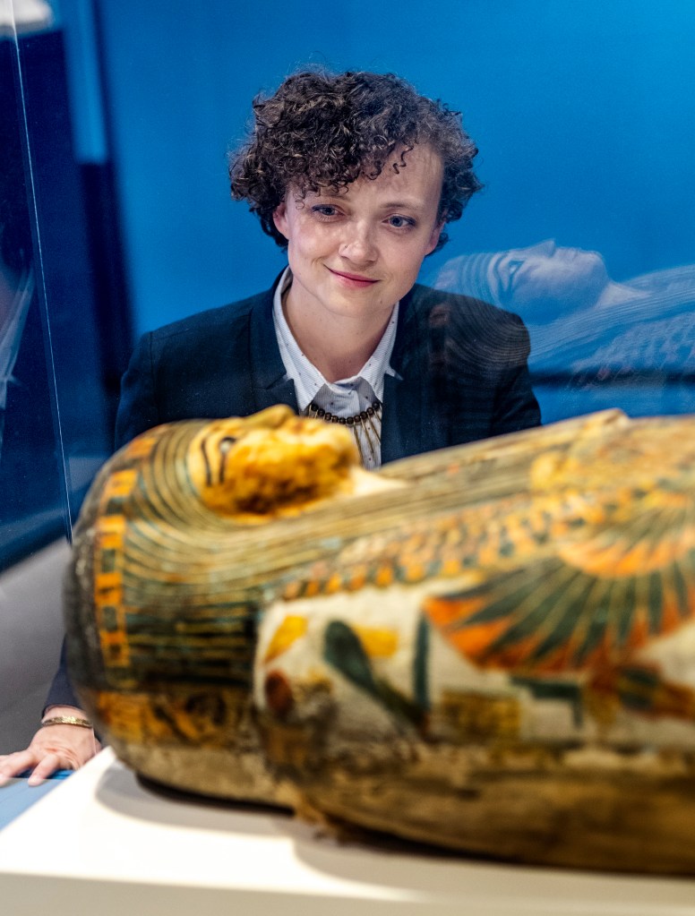 Photo of Dr. Anne Austin looking at an Egyptian sarcophagus through a glass case.