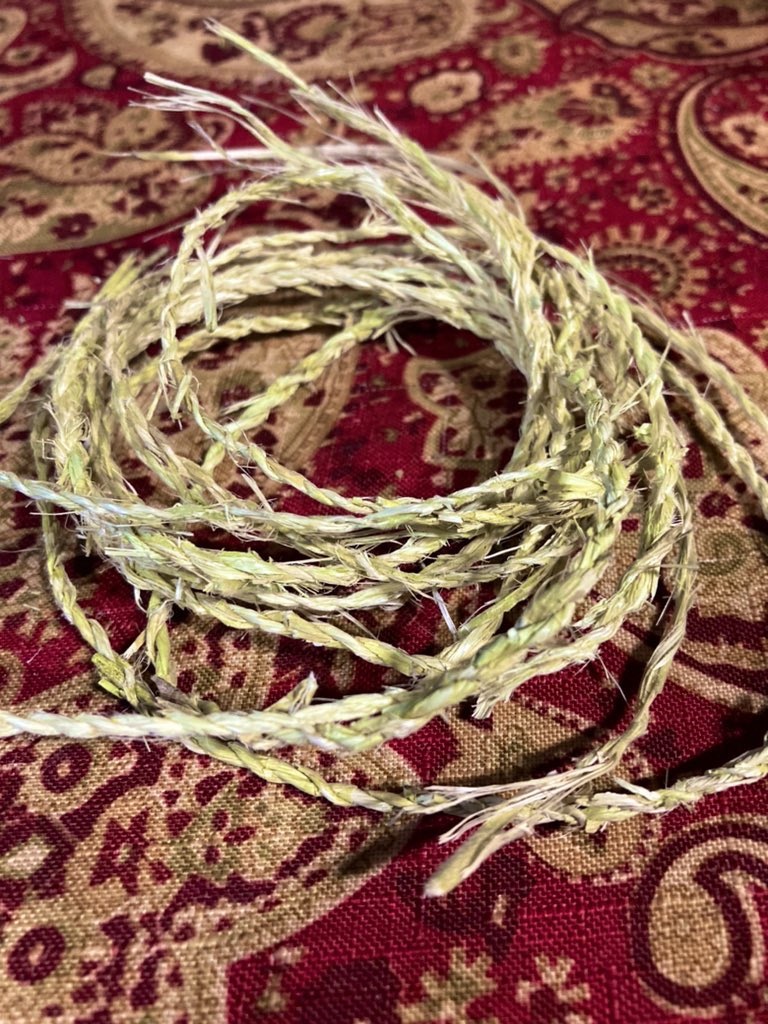 A pile of cordage made from plant fibers sits on a burgundy and gold tablecloth. 