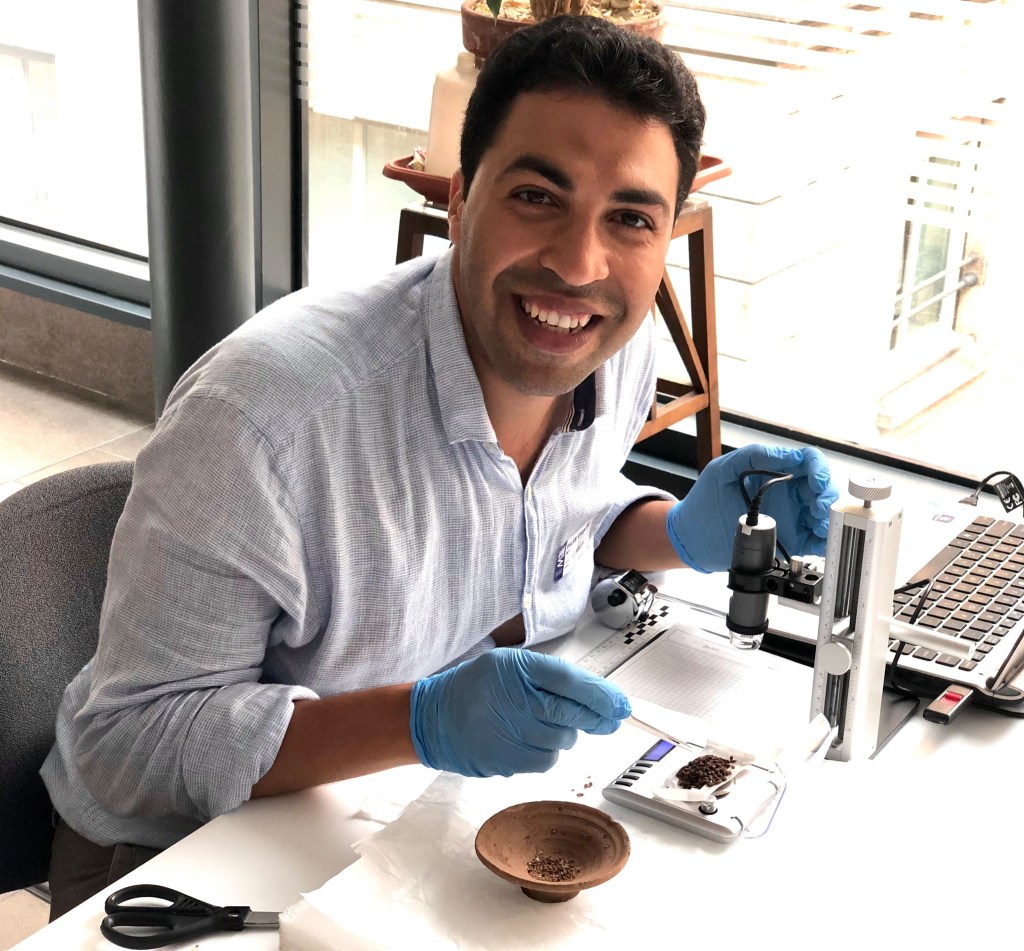 Dr. Amr Shahat at his work desk. He is smiling at the camera and wearing blue medical gloves for analysis of residue.