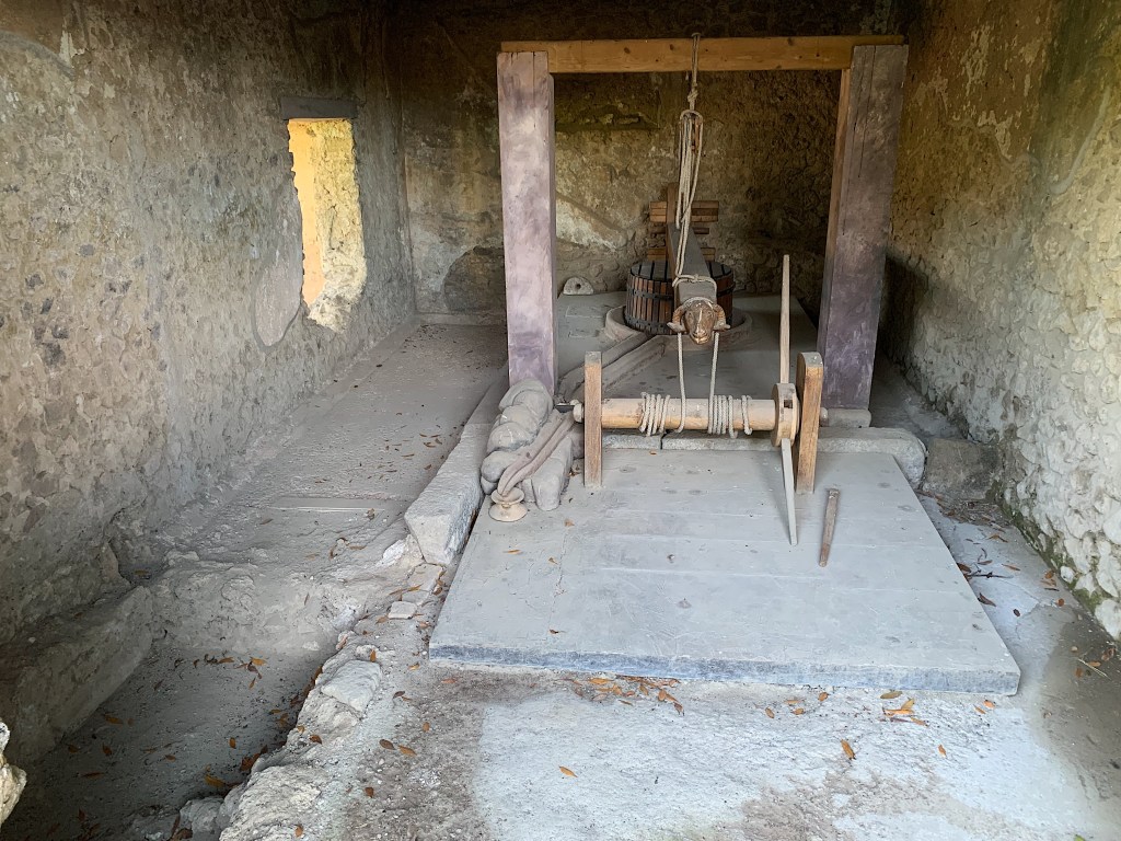 a reconstructed wine press made of wood, stone, and cordage sits inside a stone walled room