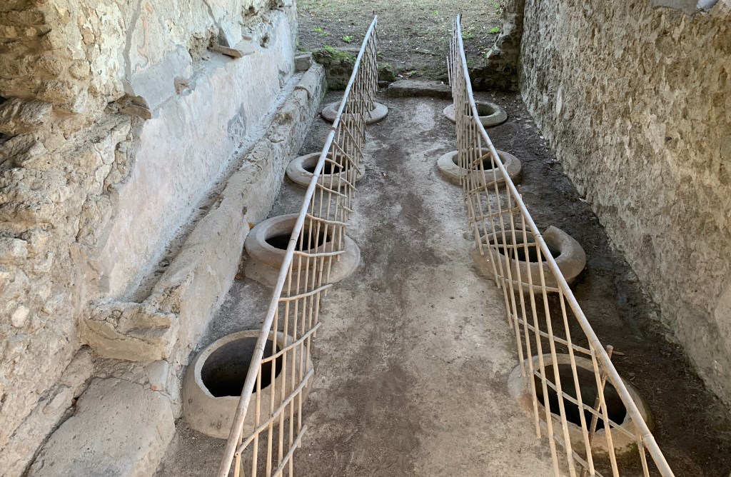 A stone wine cellar with eight visible openings in the ground beside the wine press.