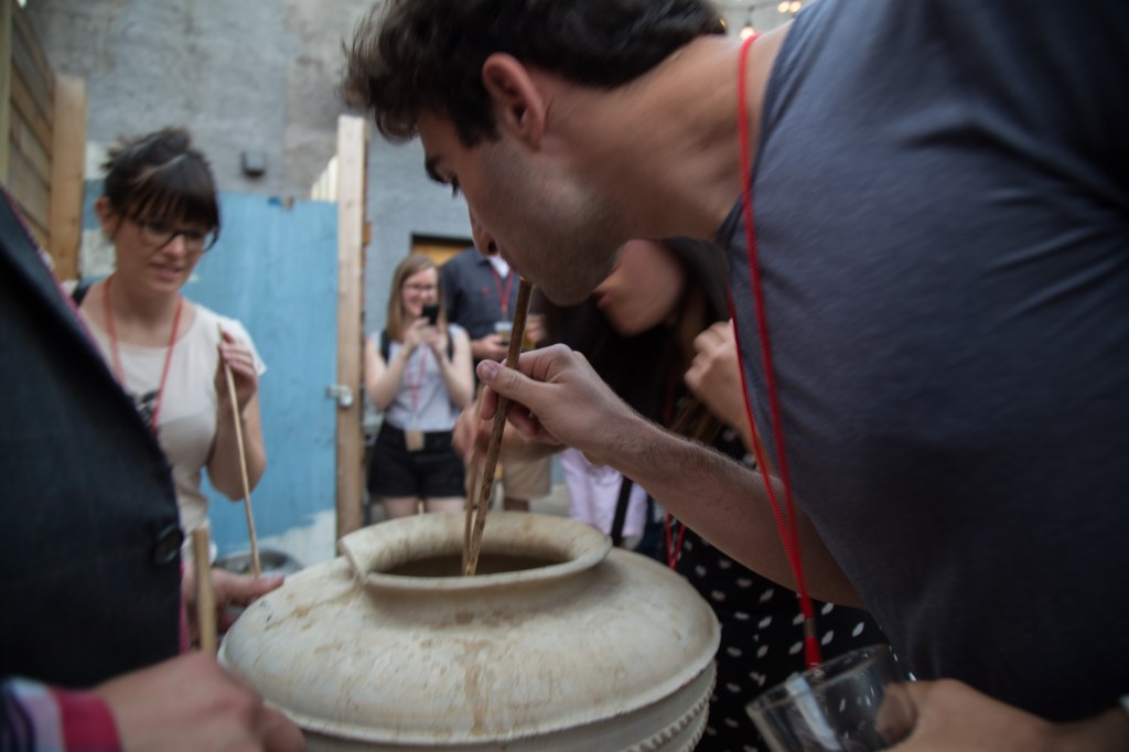 A person drinks beer from a ceramic vessel with a reed straw