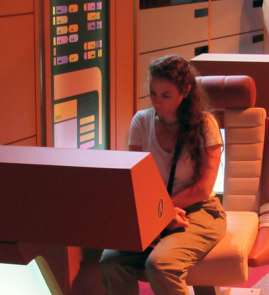 Dr. Budin sits in a chair looking at a screen in the Starship Enterprise