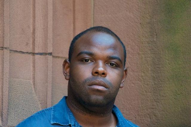 Jermaine Bryant looks into the camera. He has dark skin and dark short hair. He wears a blue denim collared shirt.