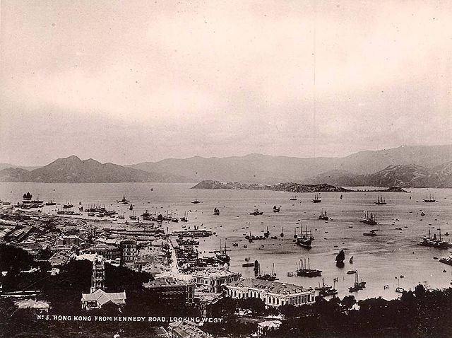 Sepia-toned photograph of harbour of Hong Kong looking west, with mountains in background, ships and harbour buildings in foreground