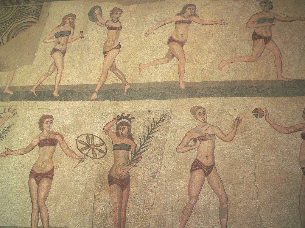 Mosaic depicting two tiers of young women exercising. Some are playing ball games, one holds a palm leaf, all of whom are wearing brassieres and loin cloths. 