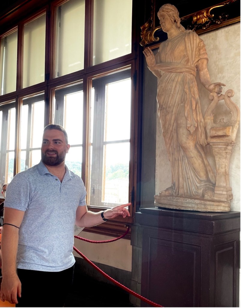 Image of Matt Coleman standing in a museum pointing to a statue