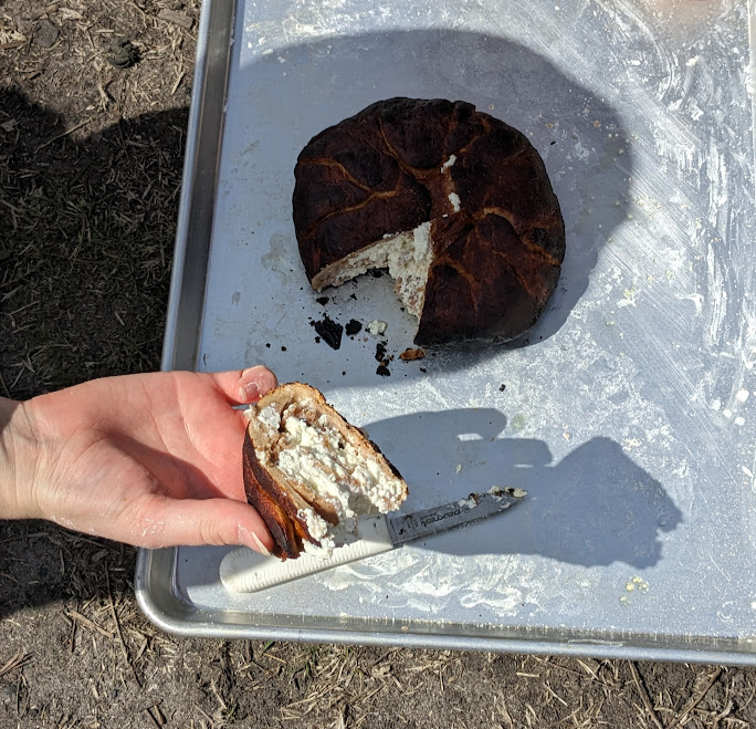 Image of a cooked placenta - a round bread with cheese; a wedge of bread has been sliced and a hand is holding up the sliced piece to see the cheese layers.