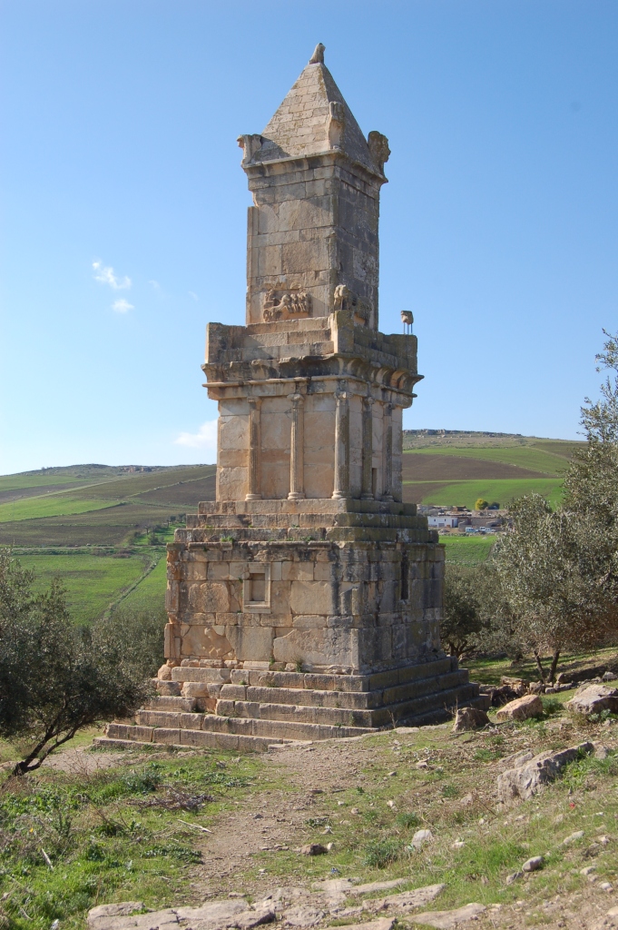 A photo of a tower tomb, which has three successively smaller squares placed on top of one another. Carved with decorations that includes chariots and columns. 