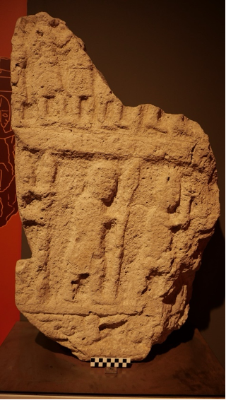 A fragment of a limestone stele with two individuals (and probably a third) in a procession.