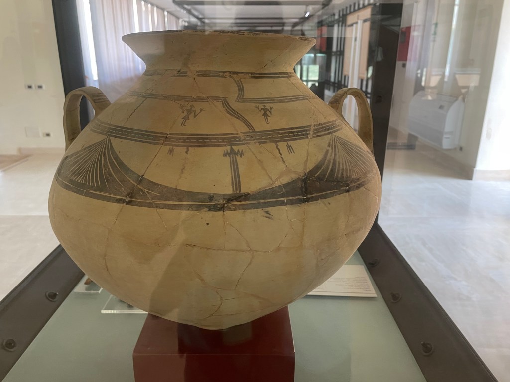 A bulbous lipped-jar with two vertical handles. It is a white-yellow colour with black decoration.