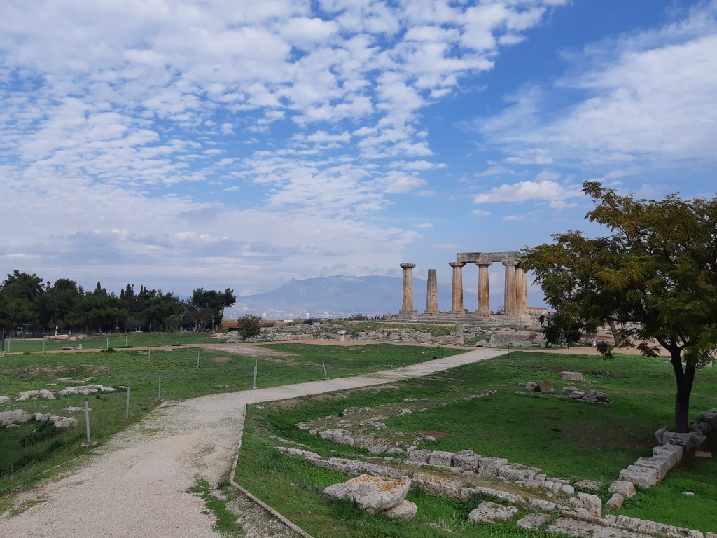 A photo of an archaeological site. In the foreground is a dirt path which leads to a temple in ruins.