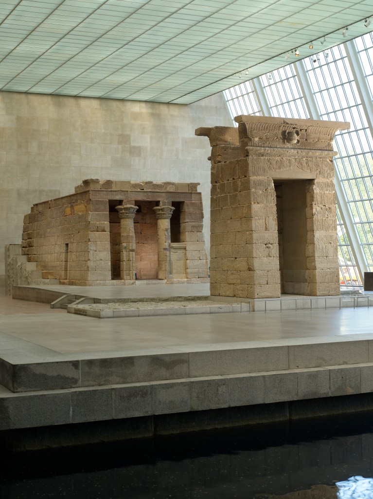 Large museum gallery with fragments of an Egyptian temple building, made out of stone, reconstructed in the center.