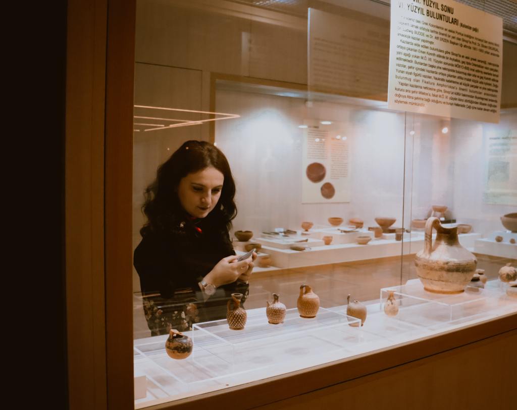 White woman with dark brown curly hair looking at several small objects in a museum display case.