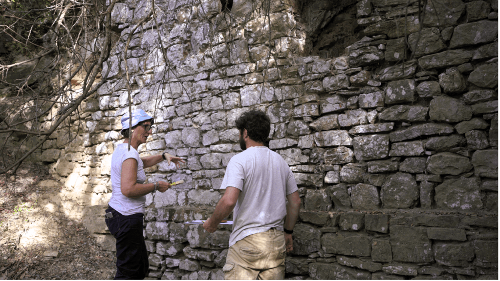 A white woman wearing a blue hat and a white man wearing a white shirt standing in front of a rock wall. 