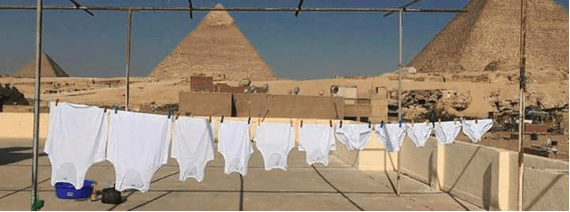 A string of white t-shirts and underwear hanging in the foreground with the pyramids in the background.