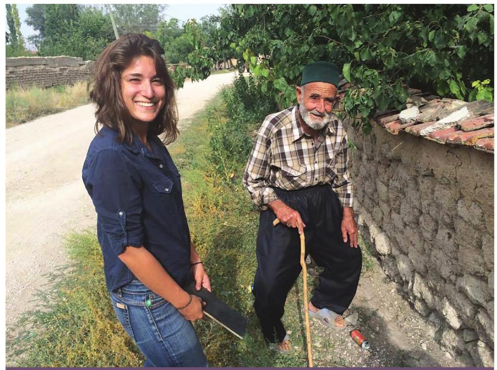 A young women stands off to the side of a road next to a local elderly man in Turkey. Both smile at the camera. 