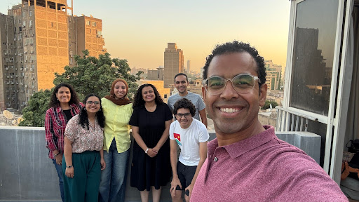 A selfie with seven individuals (4 women, 3 men) taken against a city backdrop in Egypt.