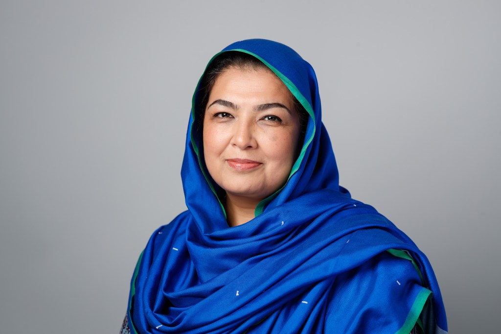 Headshot of Uzma Z. Rizvi; smiling female with a blue head covering/hijab/duppatta.