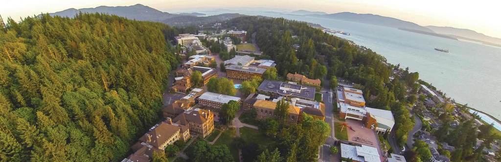 Aerial view of several buildings on a university campus, with the ocean on one side and a forest on the other.