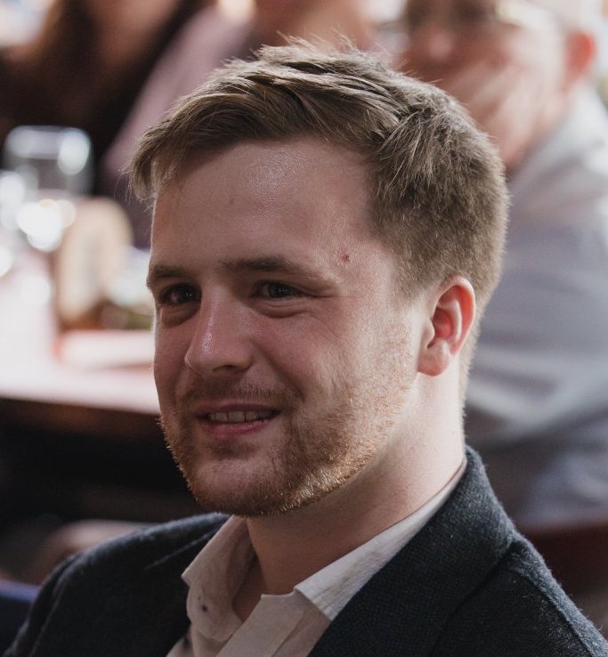 A white man with short blond hair and facial hair. 