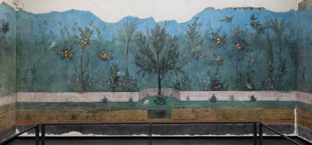 A photograph of a wall painted with an elaborate garden scene, including several fruit-bearing trees, shrubs, and a low-lying fence. 