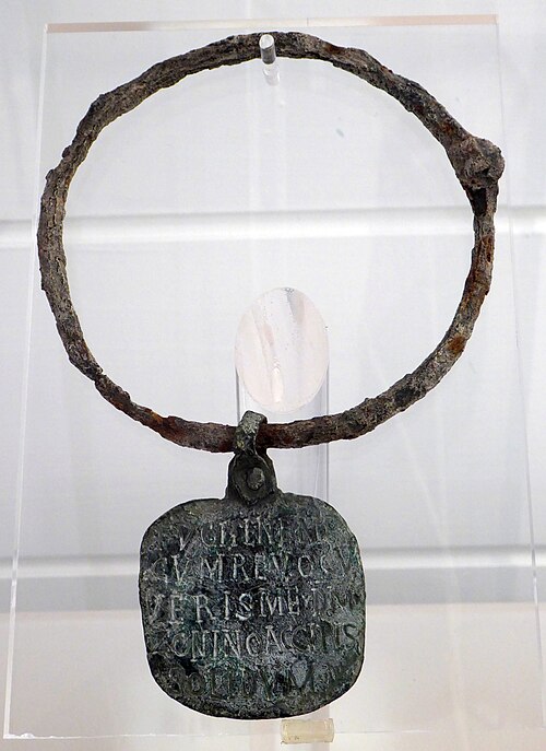 A bronze collar with a small square pendant attached. This pendant is inscribed with Latin letters.