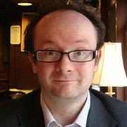 A headshot of a white man wearing glasses with a dark frame.