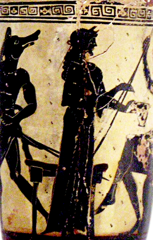 lose-up of tall vessel with white background and figures painted in black in incised details. A woman stands in a long gown holding out a drinking cup to a figure seated to her right (only the legs and one arm remain). A stool is behind her. A man with a dog’s head runs to her left. There is a meander frieze above.